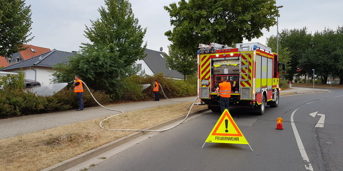 Foto: Die Feuerwehr gießt städtische Bäume in Marbach. © Stadtverwaltung Erfurt Drei Feuerwehrmänner mit Löschschlauch und einem Einsatzfahrzeug.