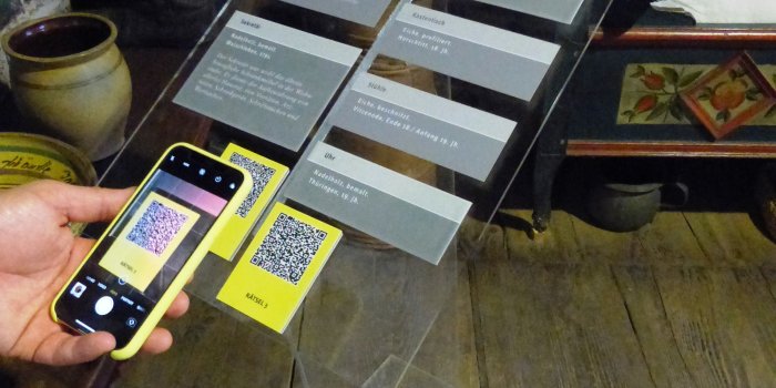 Foto: Handy vor Ausstellungsobjekt im Volkskundemuseum © Stadtverwaltung Erfurt/Volkskundemuseum Ein Handy scannt einen Code von einer Ausstellungstafel