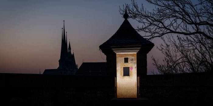 Nächtliches Bild eines beleuchteten Turms des Petersbergs mit deutlich erkennbarem Graffiti, im Hintergrund der Dom