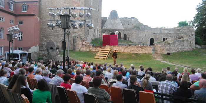 Im Hintergrund eine Burg, davor Schauspieler und Zuschauer