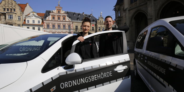 Eine Frau und ein Mann stehen vor zwei Fahrzeugen auf denen Ordnungsbehörde steht. 