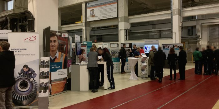 Messestände mit Besuchern in Industriehalle