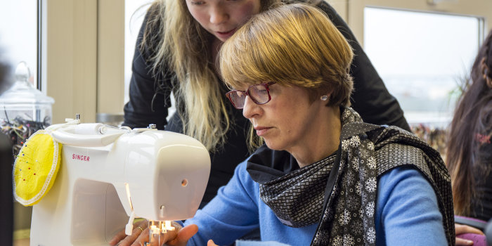 Foto: Besuch der Schülerfirma ReOli © Stadtverwaltung Erfurt Eine Dame sitzt an einer Nähmaschine, ein junges Mädchen schaut ihr zu.