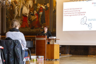 Frau am Rednerpult vor Leinwandpräsentation redet vor Publikum