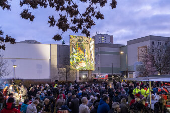 Zahlreiche Menschen stehen vor einem beleuchteten Wandmosaik