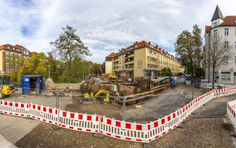 Ein Bauzaun, dahinter ein großes Rohr und Baufahrzeuge