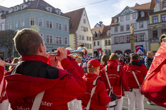 Kinder eines Fanfarenorchesters spielen auf einem Platz mit historischen Gebäuden im Hintergrund