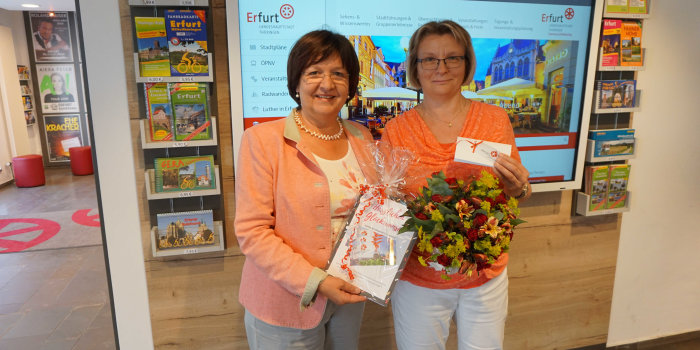 Foto: Jubiläum für den Erfurt-Gutschein © ETMG Zwei Frauen stehen nebeneinander, die rechte hält einen Blumenstrauß, die linke übergit ein Präsent.