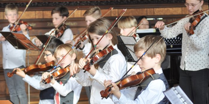 Kinder spielen mit Streichinstrumenten in einem historischen Saal.