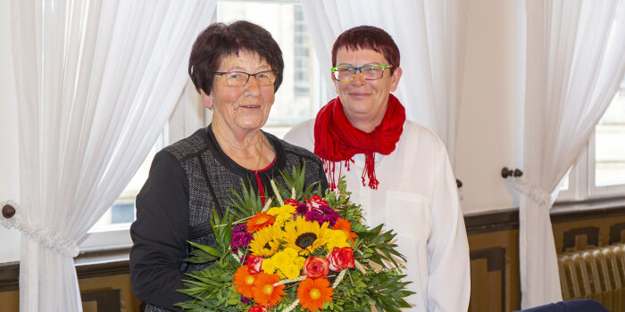 Zwei Damen stehen nebeneinander, eine Dame hält einen Blumenstrauß