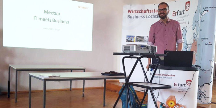 Ein Mann hält einen Vortrag mit einer Powerpoint-Präsentation im Hintergrund. 
