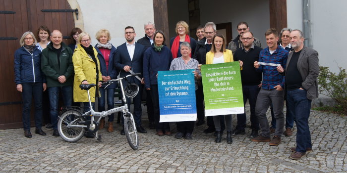 Mehrere Männer und Frauen stehen mit einem Fahrrad vor einem Gebäude und werben fürs Fahrradfahren.