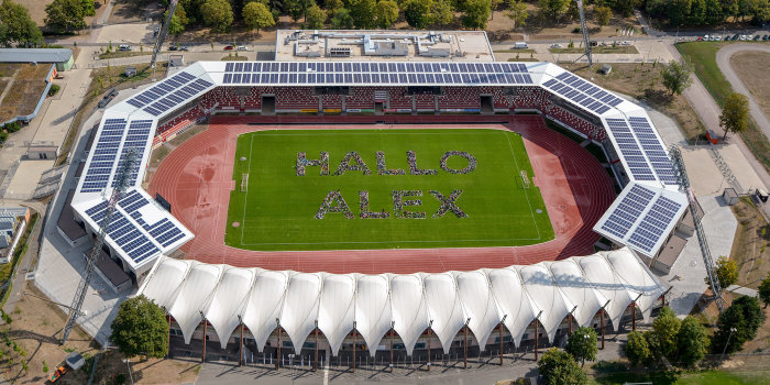 Foto: Weltraumshow im Steigerwaldstadion © Stadtverwaltung Erfurt Ein Luftbild von einem Stadion. Auf dem Rasen haben sich Kinder zum Schriftzug "Hallo Alex" formiert.