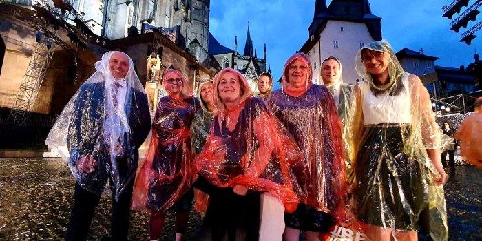 Gruppe von Personen im Regen mit Regencapes vor Kirchenensemble