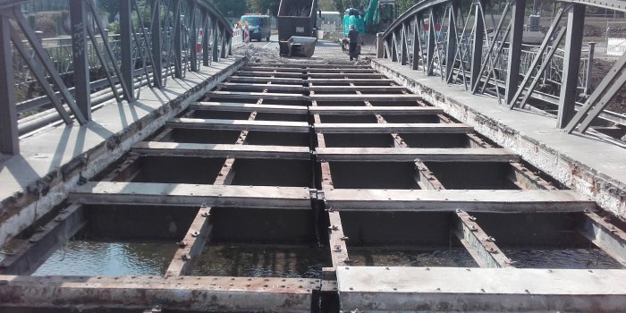 Das Gerüst einer alten Stahlbogenbrücke, das längswärts durchtrennt ist.