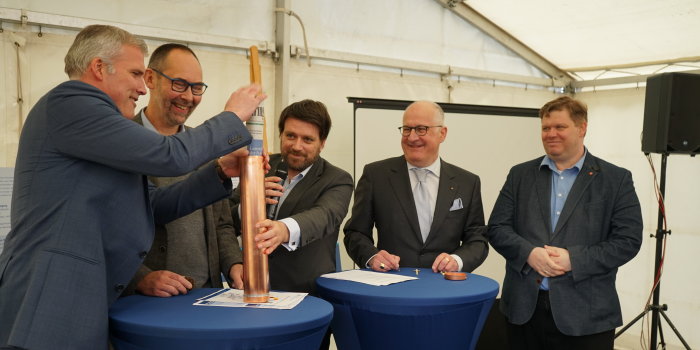 Foto: Grundsteinlegung für Schauwasserkraftwerk gelegt © Stadtverwaltung Erfurt Fünf Männer stehen an zwei Tischen und befüllen eine Kupferhülse mit Zeitdokumenten