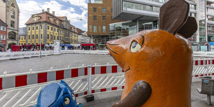 Die Kika-Figuren Maus und Elefant stehen vor rot-weißen Absperrgittern.
