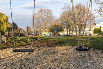 zwei Schaukeln auf einem Spielplatz, im Hintergrund weitere Spielgeräte