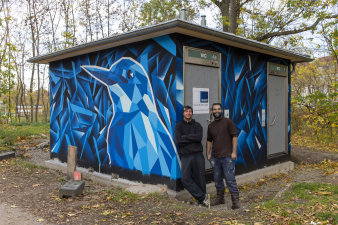 zwei Männer stehen vor einer Toilettenanlage, dessen Fassade ein Graffiti schmückt