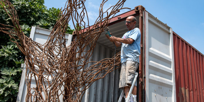 der nachgebildete Baum aus Metall wird in den Container gelasen