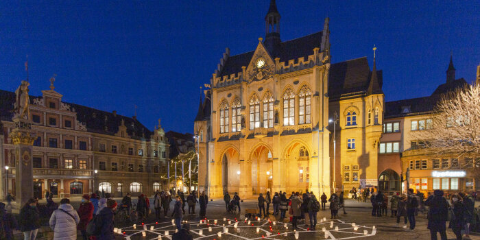 das erleuchtete Erfurter Rathaus in der Dämmerung, im Vordergrund Kerzen auf dem Boden und mehrere Menschen