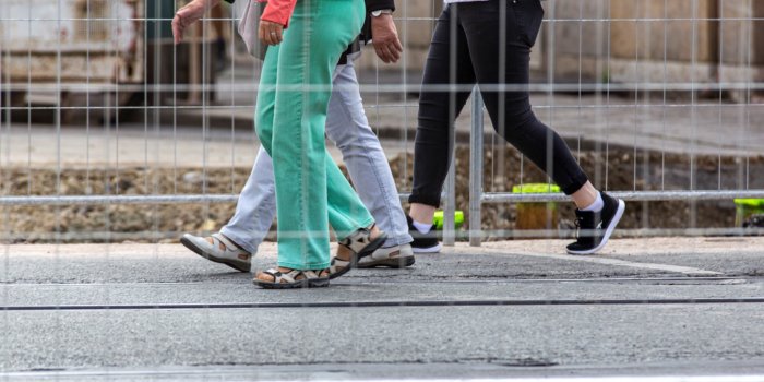 Drei Personen laufen hinter einem Bautzaun über Asphalt.