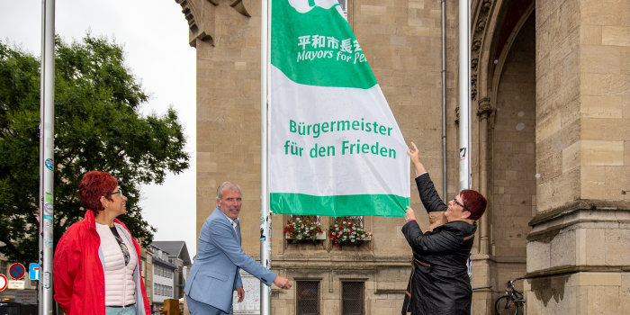 Eine Mann und eine Frau hissen eine Fahne. Auf dieser steht: Bürgermeister für den Frieden. 