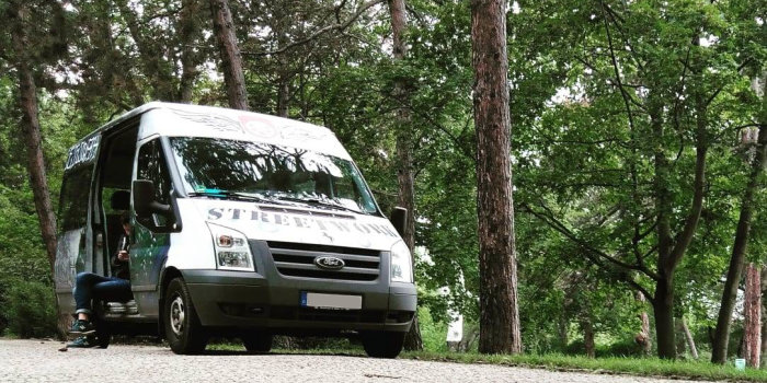 ein Transporter mit offener Schiebetür, in der ein Mensche mit dem Handy in der Hand sitzt