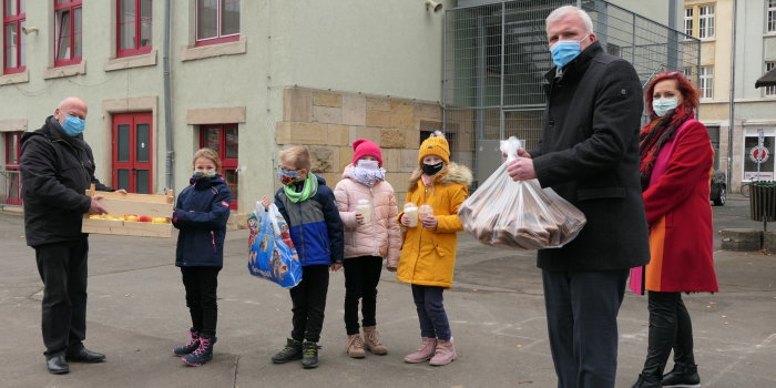 Zwei Männer übergeben Gebäck in Tüten an die Schülersprecherin