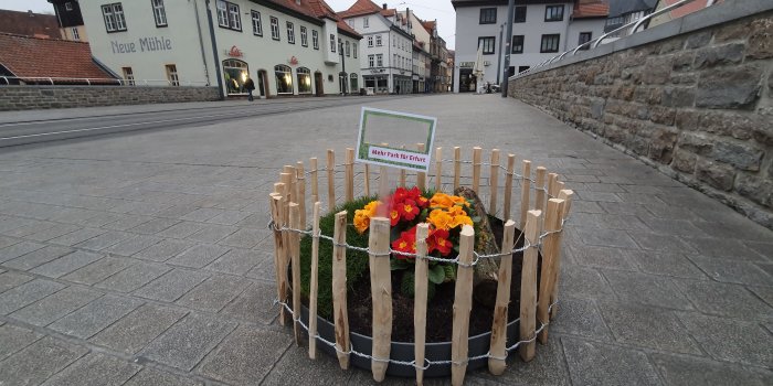 ein breiter Gehweg mit einem kreisrunden, eingezäunten Blumenbeet