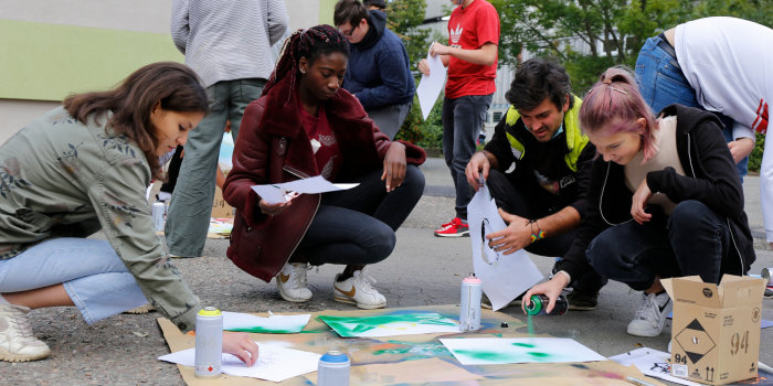 ein Mann und drei Mädchen sitzen gemeinsam vor verschiedenen Blättern Papier und gestalten sie mit Spraydosen