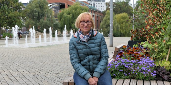 Eine Frau sitzt auf einer Bank vor dem Brunnen am Theater