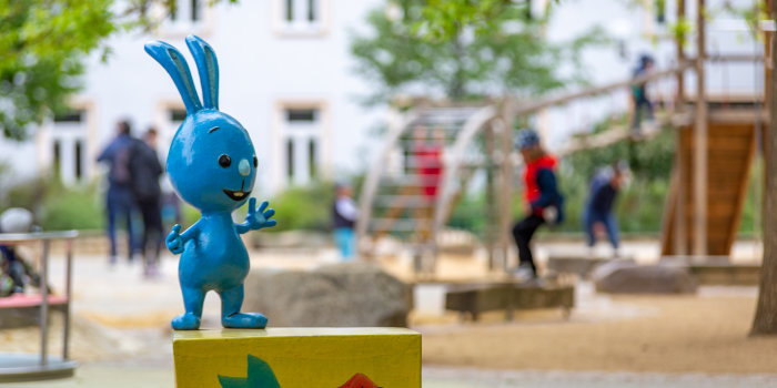 Foto: Kikaninchen Spielplatz Krämerbrücke © Stadtverwaltung Erfurt eine blaue Hasenfigur vor einem belebten Spielplatz
