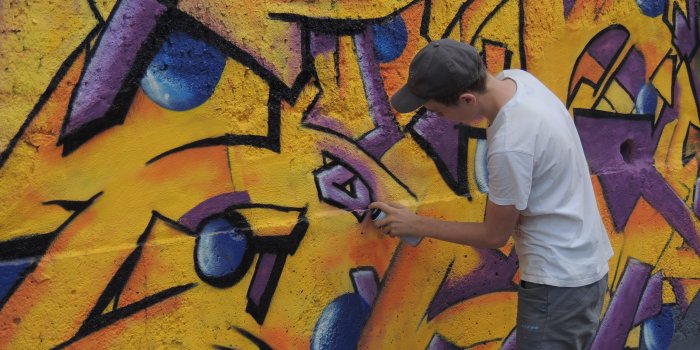 ein Kind sprüht ein Graffiti an eine Wand