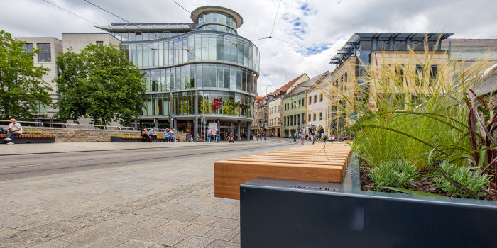 mit Bepflanzungen kombinierte Bänke stehen auf breiten Gehwegen entlang einer Straße in der Innenstadt