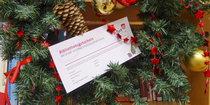 ein Bibliotheksgutschein in weihnachtlicher Dekoration mit Tannenkranz