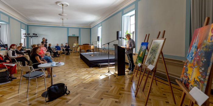 Foto: Federlesen 2020 © Stadtverwaltung Erfurt ein Mann steht an einem Saal an einem Pult, einige Zuhörer sind ihm zugewandt