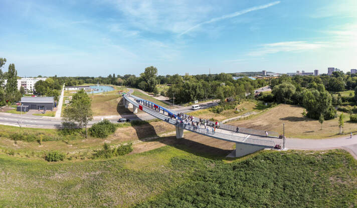 Eine Luftaufnahme von einer Brücke mit einem blauen Brückenbogen über eine Straße.