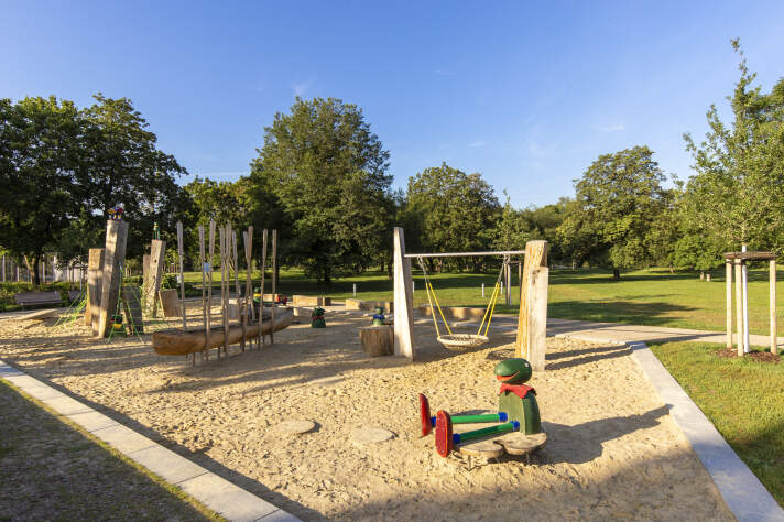 ein Kinderspielplatz mit verschiedenen Spielgeräten und einer Frosch-Figur im Vordergrund