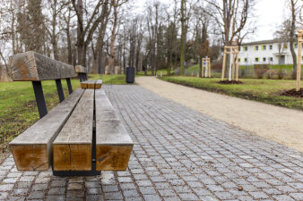 eine Parklandschaft, im Vordergrund eine Bank an einem Weg