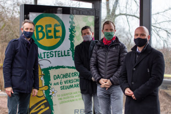 Vier Männer stehen ein einem Buswartehäuschen.