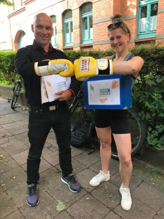 Mann und Frau stehen nebeneinander, sie haben jeweils an einer Hand Boxhandschuhe, die sie aneinanderhalten