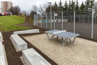 eine Fläche neben einem Bolzplatz mit Sitzblöcken aus Beton und einer Tischtennisplatte