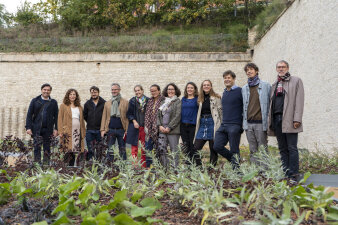 ein Gruppenfoto mit zwölf Menschen zwischen Beeten und hohen Mauern