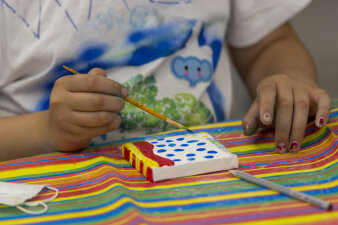 Ein Kind bemalt mit blauer Acrylfarbe eine kleine Leinwand. Auf der Leinwand sind blaue Punkte.