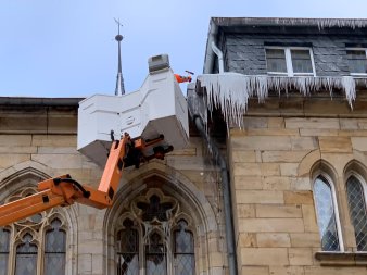 Ein Mann in einem Hubsteiger entfernt an einem Dach Eiszapfen.