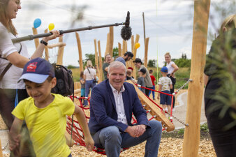 Erfurts Oberbürgermeister Andreas Bausewein wird auf einem Spielplatz interviewt, ein Kind rennt durch das Bild