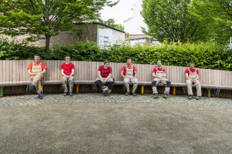 sechs Männer sitzen auf einer langen Holzbank