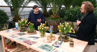 Zwei Männer im Gespräch an einem Tisch mit Blumen 