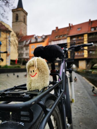 Foto: Puffbohnen-Gewinnspiel zum Stadtradeln © Stadtverwaltung Erfurt eine Plüsch-Puffbohne auf dem Gepäckträger eines Fahrrads, im Hintergrund die Erfurter Krämerbrücke